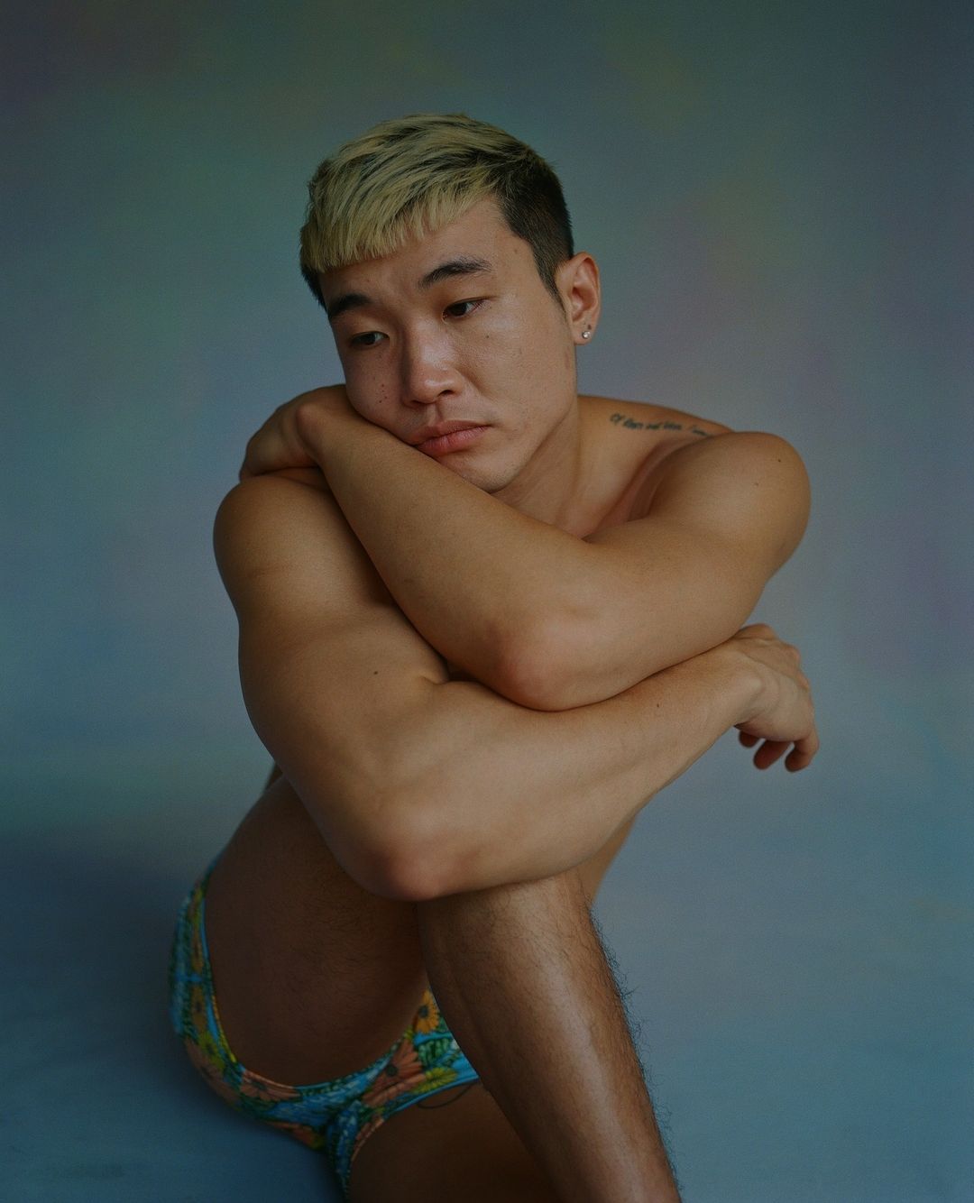 Portrait of young East Asian man with blonde-tipped hair posing against a grey seamless backdrop