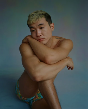 Portrait of young East Asian man with blonde-tipped hair posing against a grey seamless backdrop