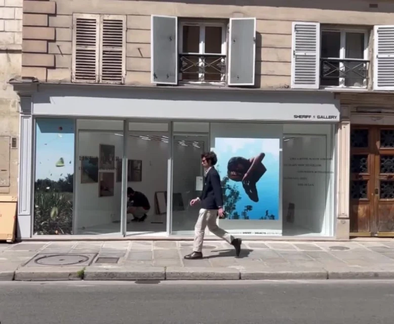 Man walking outside Sheriff Gallery with contemporary art visible through glass windows in an urban setting on a sunny day.