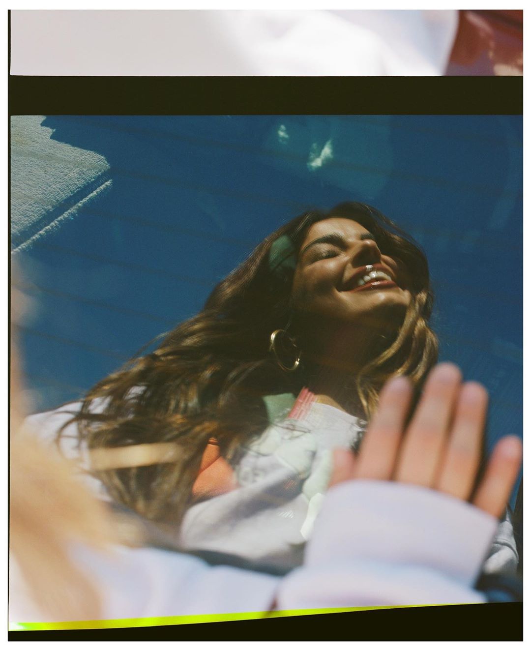 Smiling woman with long hair, wearing hoop earrings and a green headband, in a car with her hand visible on the window.