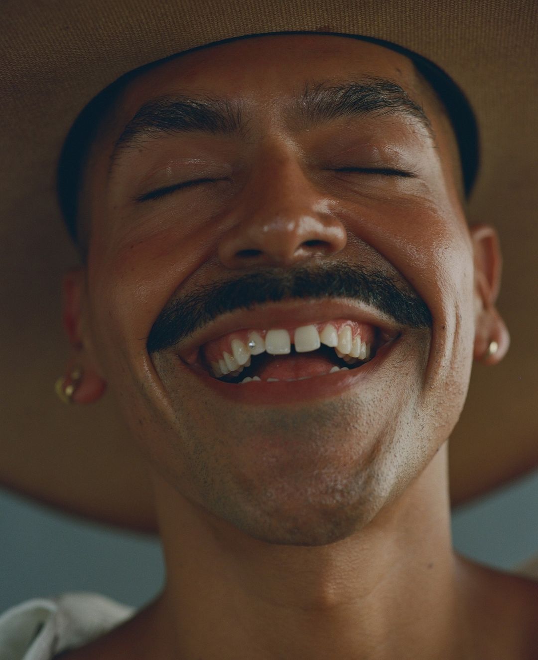 Extreme close up portrait of laughing man wearing a wide brimmed hat and small stud earrings