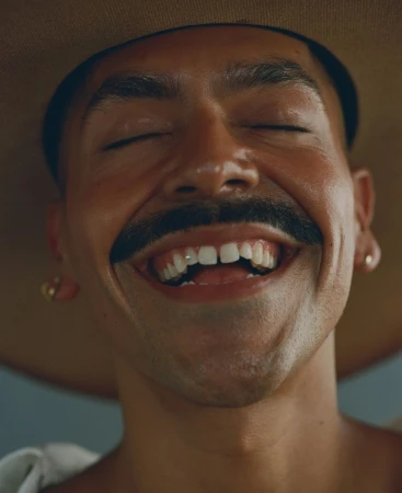 Extreme close up portrait of laughing man wearing a wide brimmed hat and small stud earrings