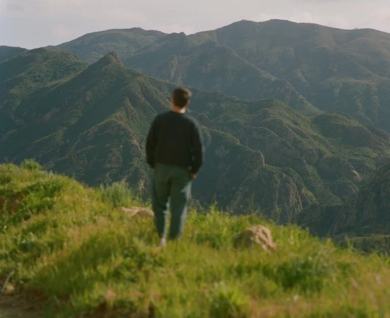 Man standing on a grassy hill overlooking a vast mountainous landscape by photographer Daniel Jack Lyons