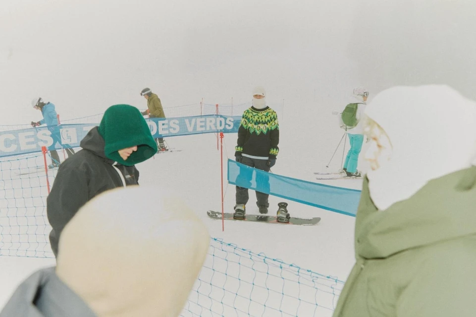 Several skiers and snowboarders are on a snow-covered mountain with a slight fog and blue safety nets in the background.