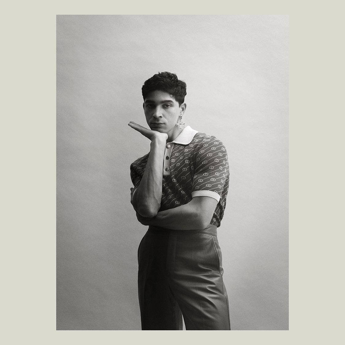Portrait of a man in a patterned polo shirt with his hand under his chin against a plain studio background.