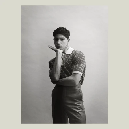 Portrait of a man in a patterned polo shirt with his hand under his chin against a plain studio background.