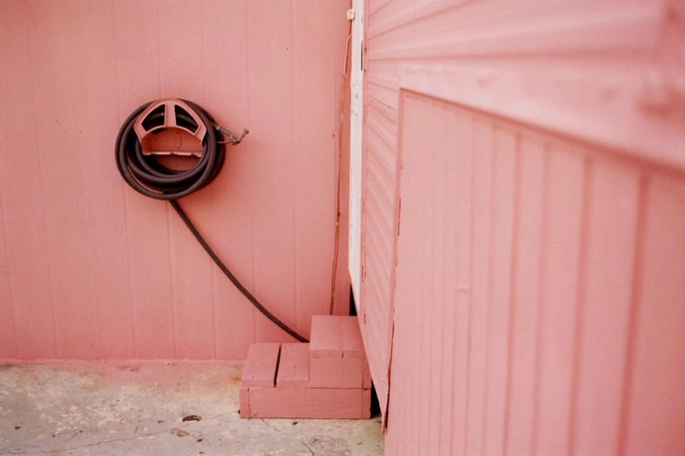Exterior of a building featuring a pink wall, a neatly coiled black hose mounted on a bracket, and small wooden steps.