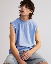Man with dark curly hair wearing a blue sleeveless t-shirt and denim shorts against a plain white background.