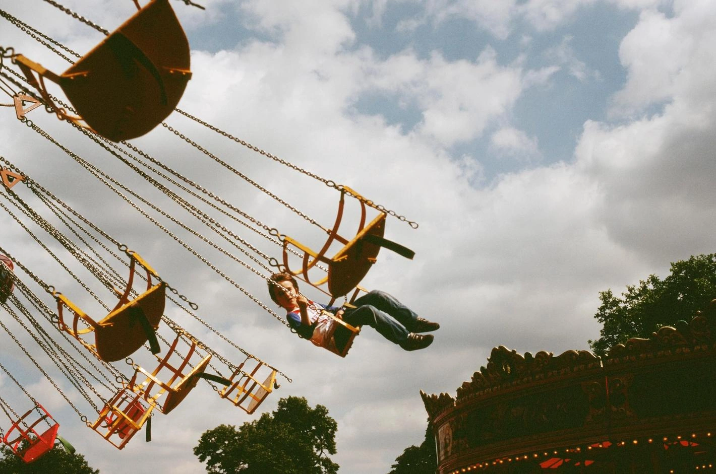 A person riding a swing on a carnival swing ride against a partly cloudy sky, captured by Lorenz Schmidl.
