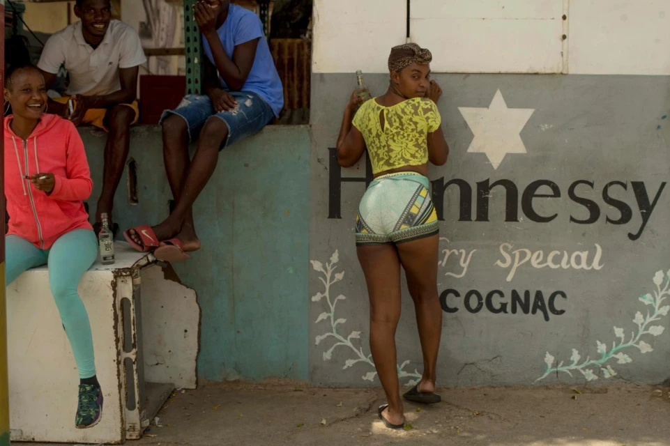Group of people posing near wall with Hennessy Cognac advertisement, outdoors in daylight, wearing casual clothing, smiling and laughing.