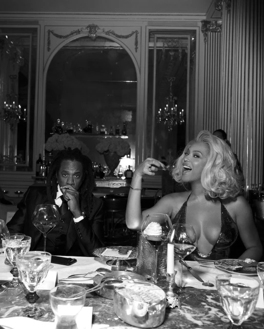 Black and white photo of a smiling adult woman and an adult man seated at a formal dining table with crystal glassware.