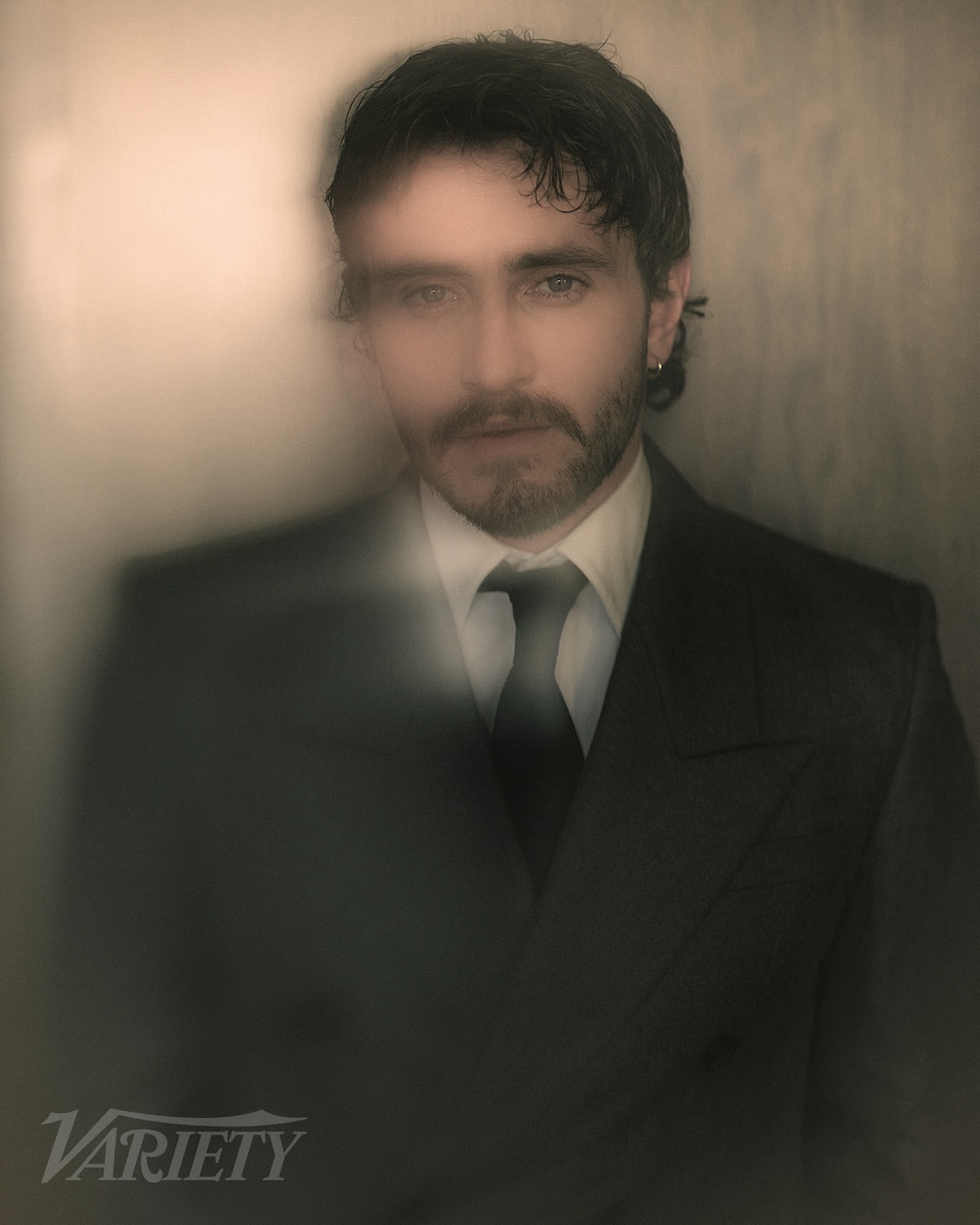 Portrait of a handsome adult male wearing a suit and tie in a studio setting with soft lighting and diffused focus.