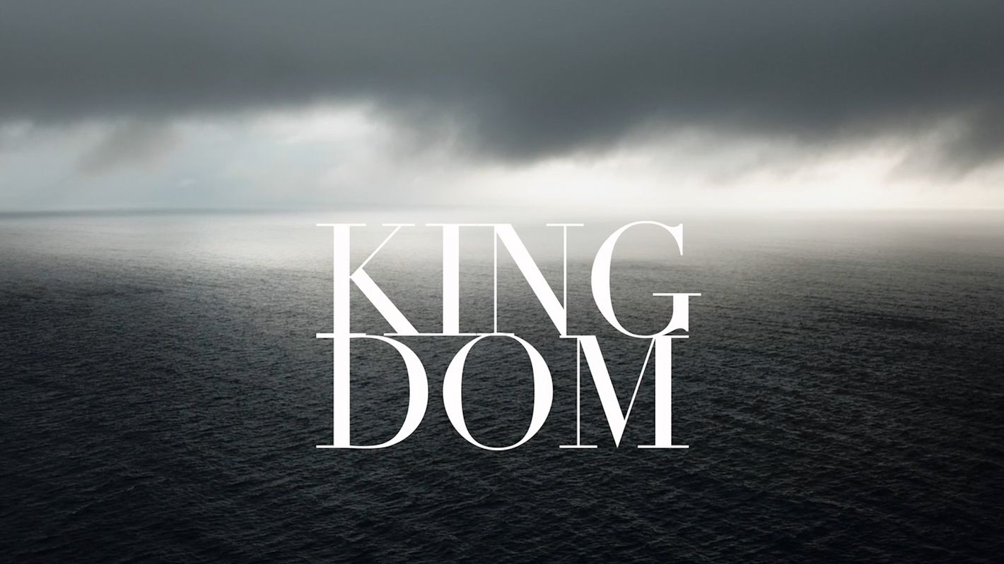 Aerial view of a dark, rippled ocean beneath a cloudy sky, overlaid with large white letters spelling out the word 'KINGDOM'.