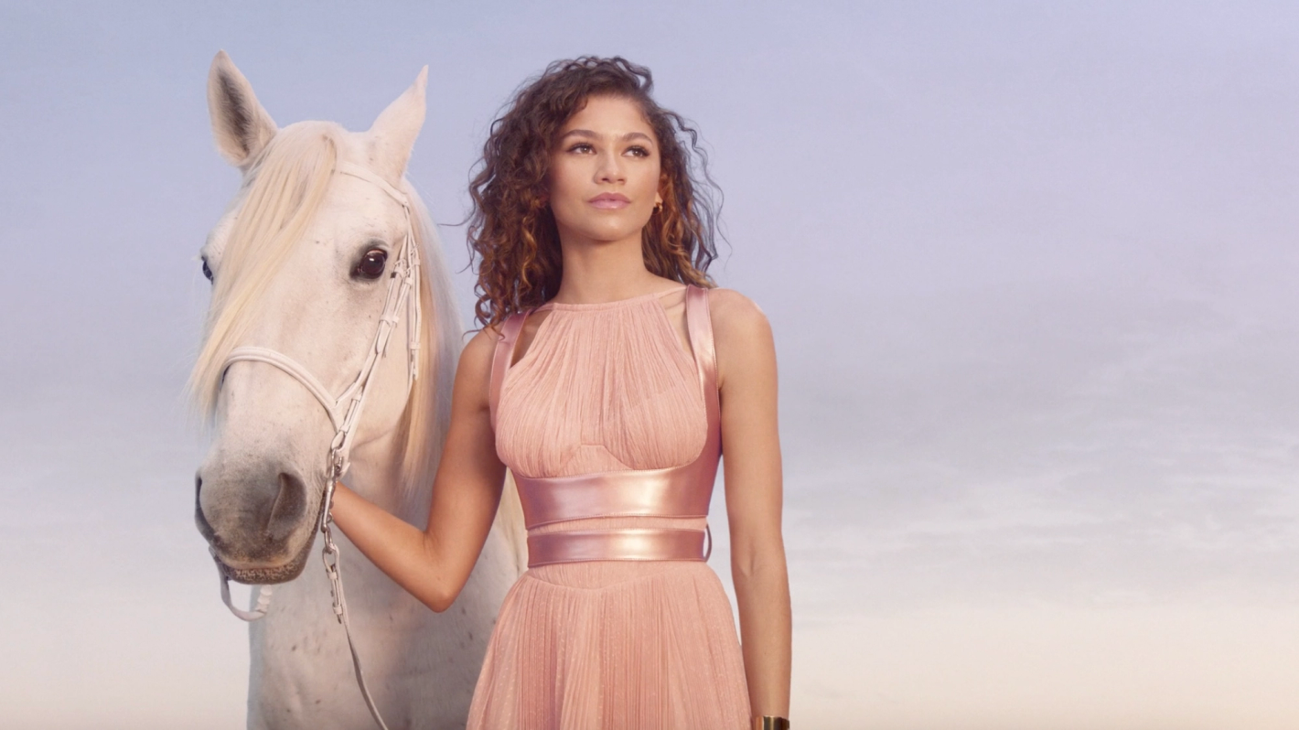 Woman in pink dress with white horse in outdoor fashion shot, soft focus, light airy sky background.