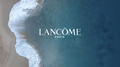 Aerial view of ocean waves breaking on a sandy beach with Lancome Paris logo overlaid