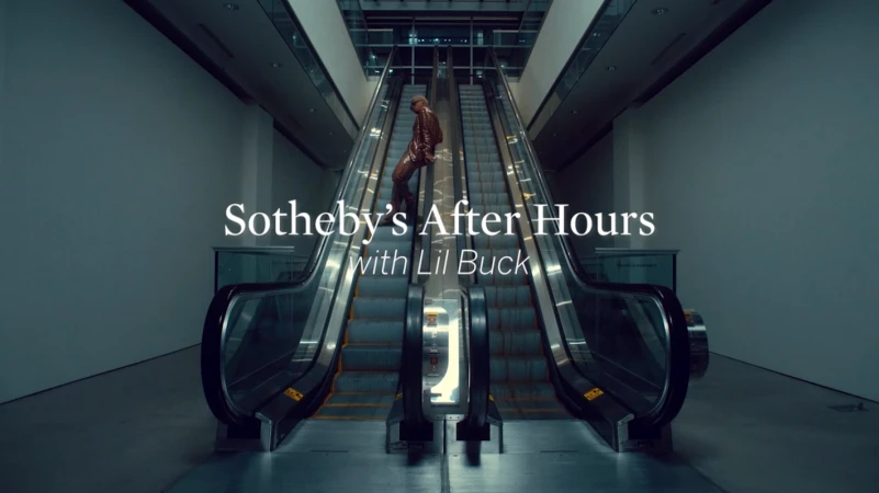 Man in a brown suit stands on an escalator in a modern building with white text overlayed on the scene, Sotheby's After Hours with Lil Buck.