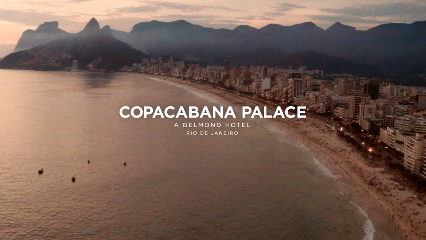 Aerial view of Copacabana Beach in Rio de Janeiro, Brazil, with cityscape and mountains under a dusky sky at twilight.