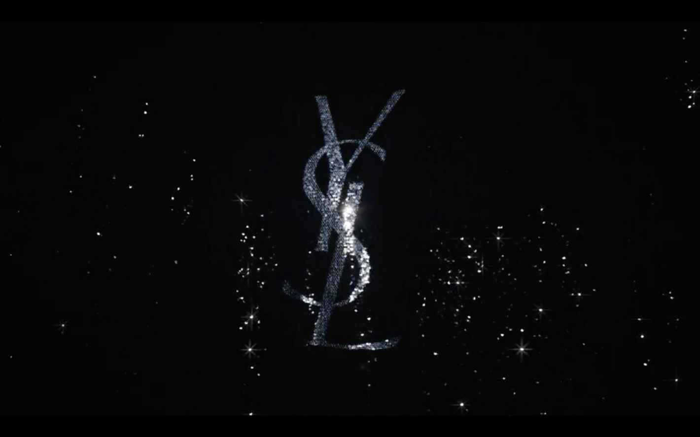 Glittering YSL logo on black background with twinkling bokeh. Sparkly luxury design for fashion, beauty, and entertainment brands.