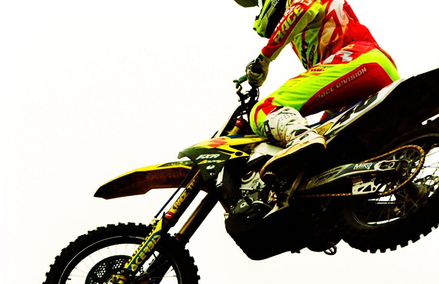 Motocross racer in mid-air, riding a yellow bike, wearing bright red, yellow, and white racing gear against a white background.