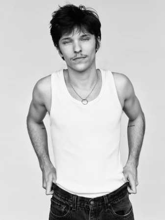 Monochrome portrait of a young man wearing a white tank top and dark jeans against a seamless background, photographed by Remi Pujol.