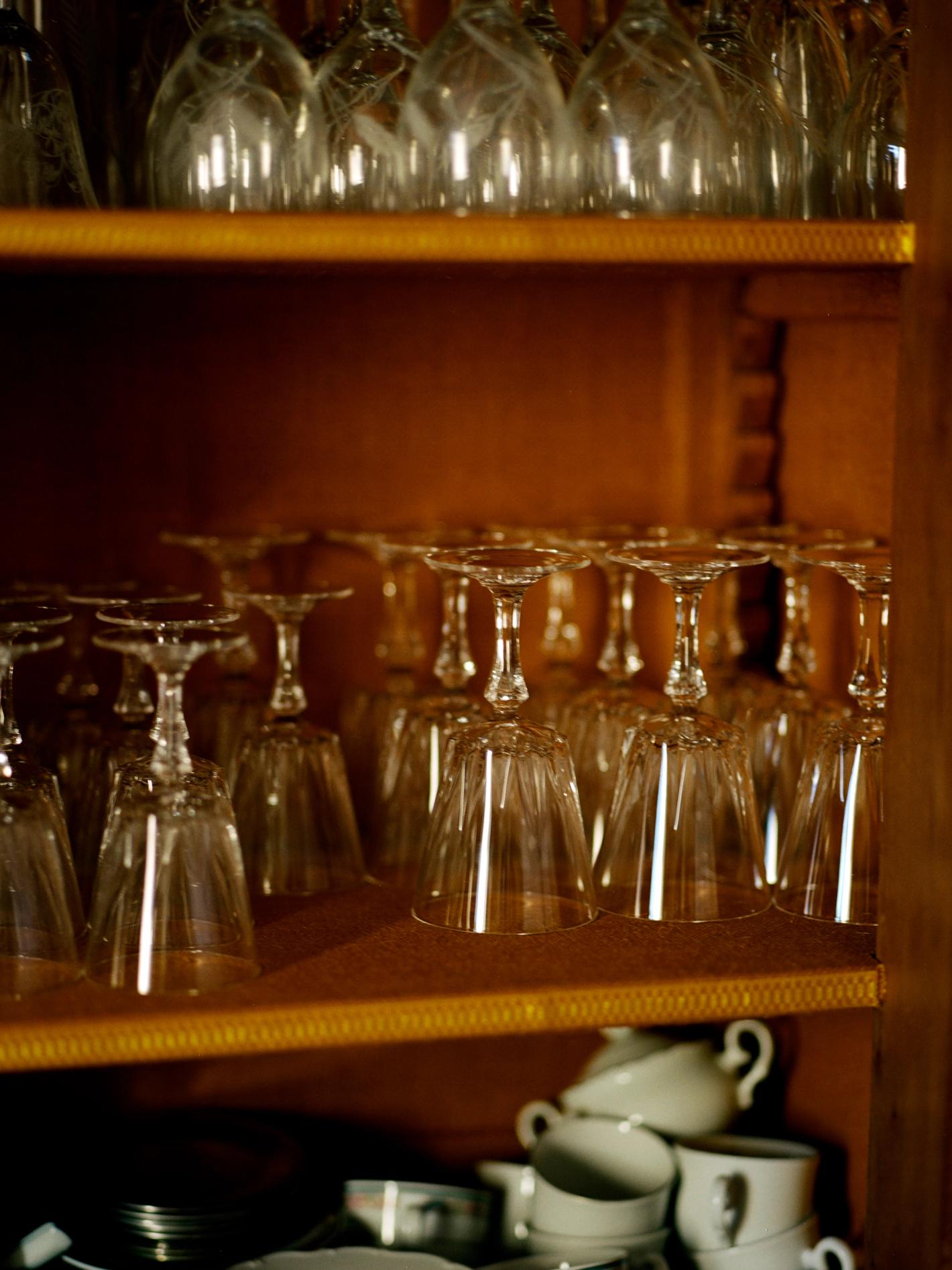 Wine glasses displayed on shelves in wooden cabinet, illuminated by warm lighting, creating a cozy ambiance.