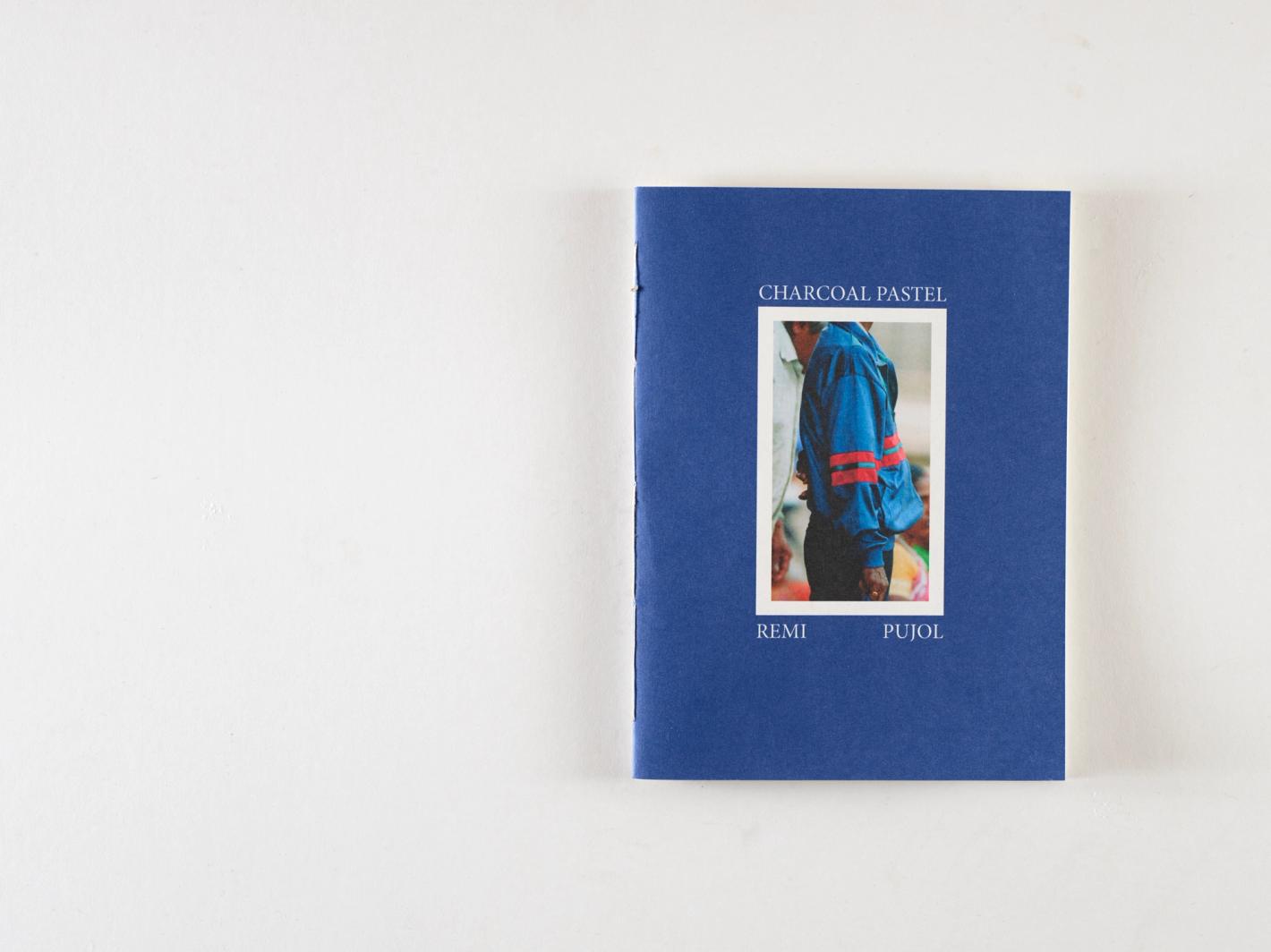 Close-up of a blue book cover with a photo of a person wearing a blue sweatshirt. The text reads 'Charcoal Pastel, Remi Pujol'.