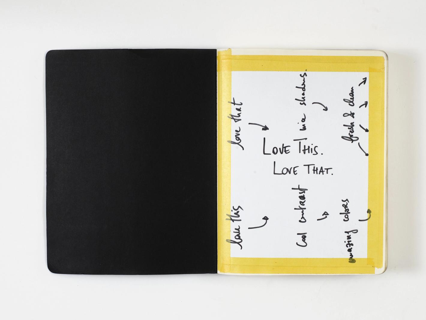 Open notebook with one black page and one white page with handwritten notes taped with yellow tape on a white surface.