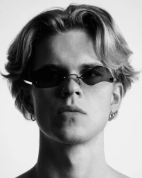 Close-up portrait of a young man wearing tinted rimless sunglasses against a bright white background