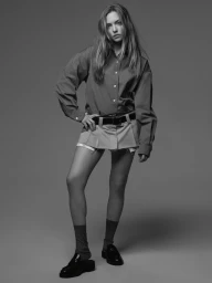 Monochrome portrait of a woman wearing a button-down shirt and mini skirt against a neutral backdrop