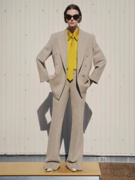 Model wearing oversized beige suit, yellow shirt, tie, and sunglasses standing outside in New York styled by Elissa Santisi.