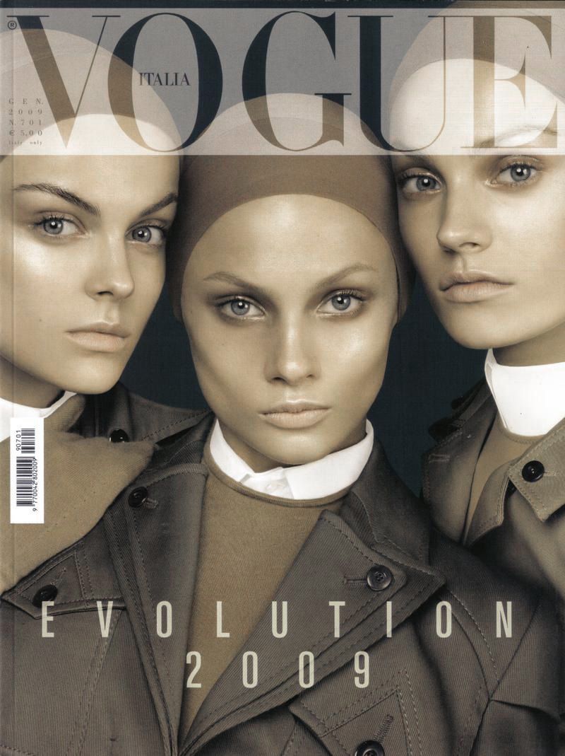 Vogue Italia cover featuring three adult female fashion models with similar makeup and haircuts, wearing trench coats, against a dark background.