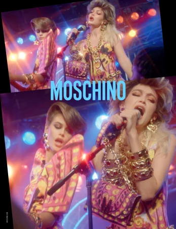 Two fashion models, one with blonde hair and one with brunette hair, sing into microphones with vintage glam style against a lighting backdrop.
