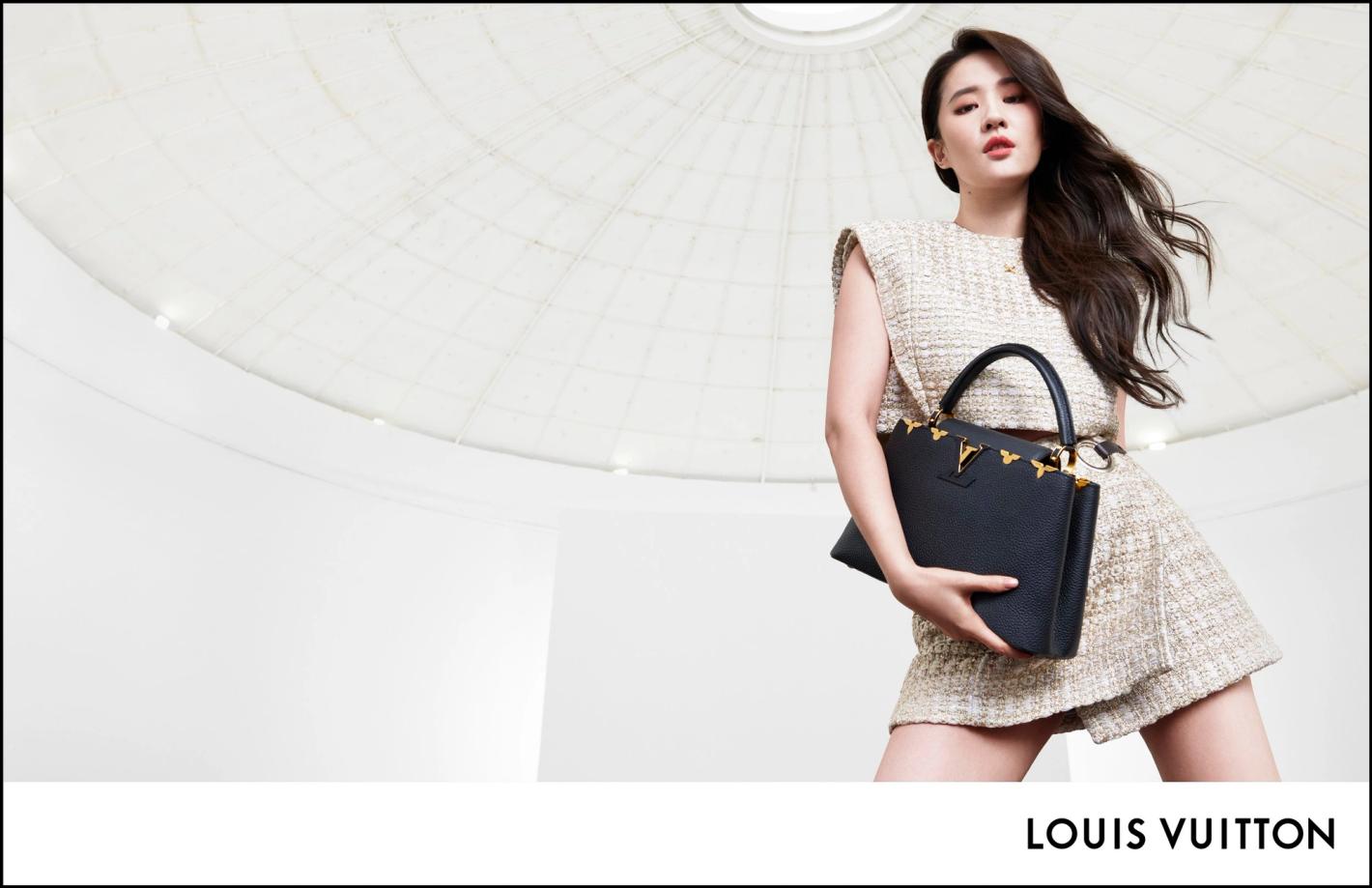 Elegant Asian woman poses with a black Louis Vuitton bag against a bright white dome background in a sophisticated fashion shot.