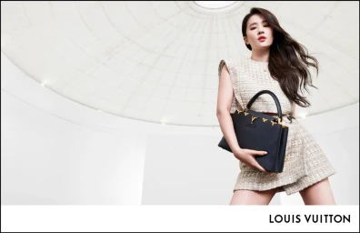 Woman in cream tweed crop top holding a black leather handbag beneath an arched white ceiling, directed by Jason Duzansky.