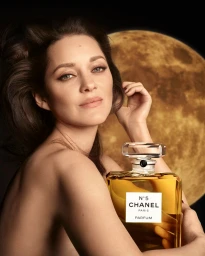 Marion Cotillard holding a large Chanel No 5 perfume bottle in front of a golden moon backdrop.