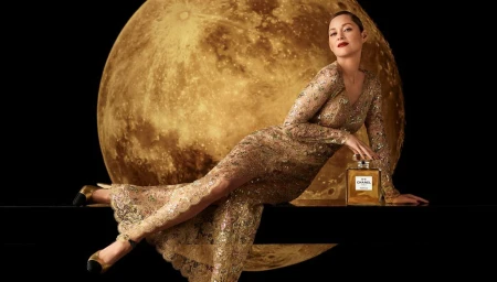 Marion Cotillard in a shimmering gold lace gown reclining against a giant illuminated moon background with a Chanel No. 5 perfume bottle.