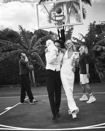 Black and white portrait of a couple walking on a basketball court, styled by Dena Giannini, holding small dogs.