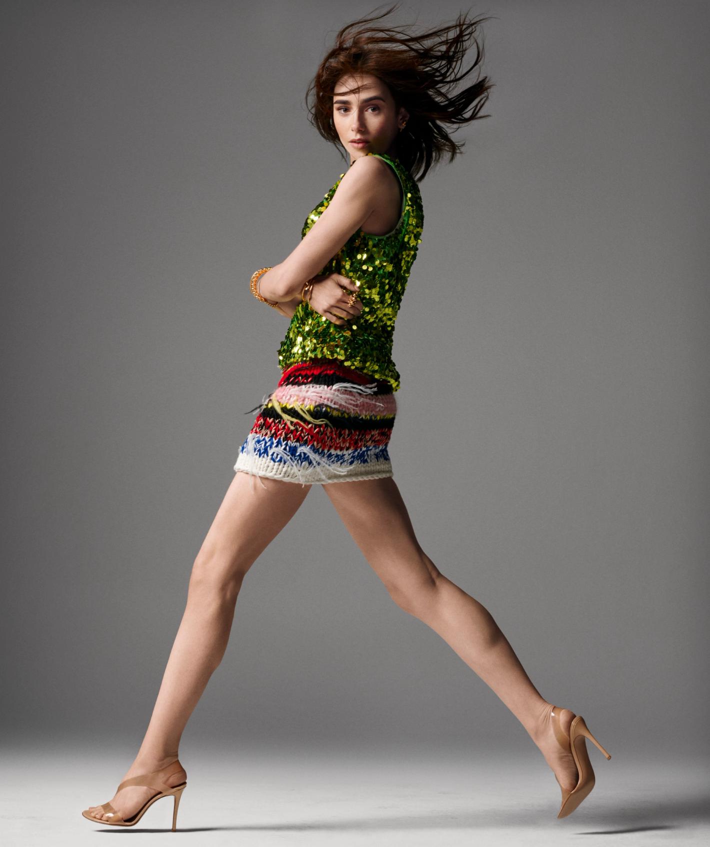 Model in green sequin top and patterned mini skirt leaping against a plain grey studio backdrop