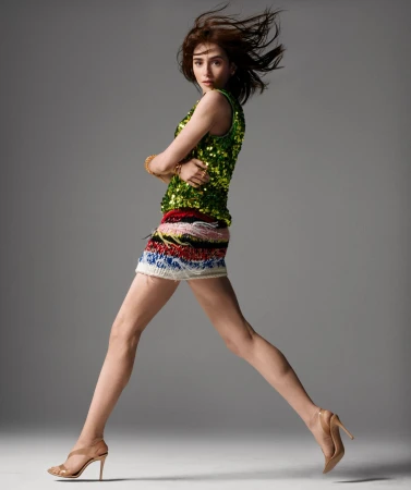 Model in green sequin top and patterned mini skirt leaping against a plain grey studio backdrop