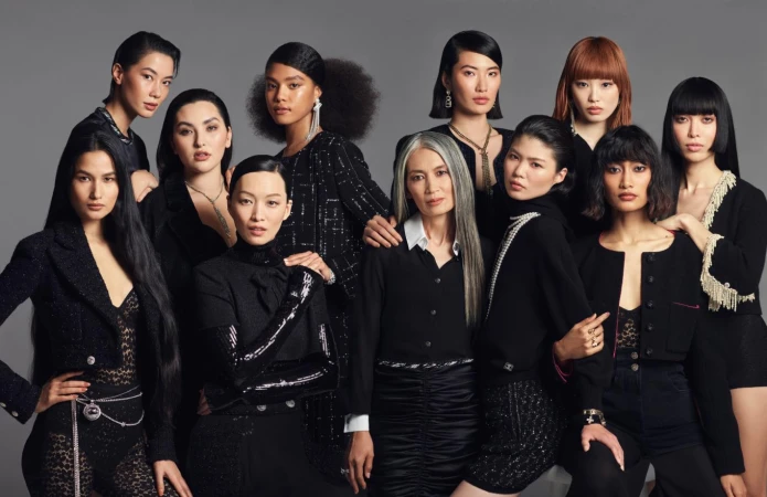 Diverse group of ten adult women in fashionable black clothing, jewelry and elegant hairstyles, posing against a neutral grey backdrop.