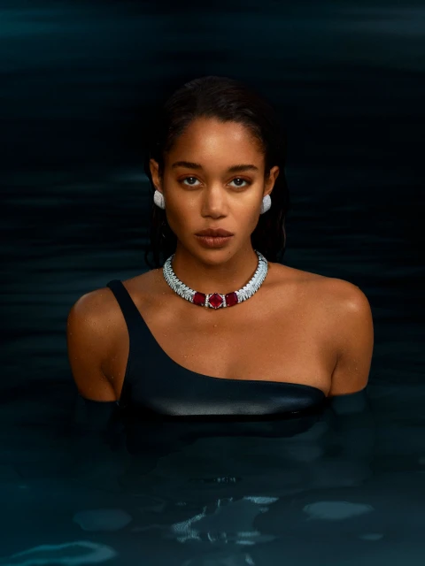 Adult female with dark hair and one shoulder swimsuit posing in water wearing a silver necklace with red gems and white stud earrings.