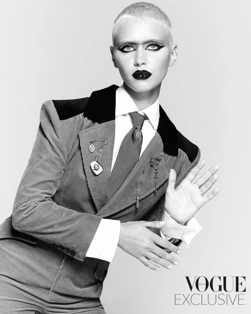 A striking black and white portrait captures a fair-skinned adult woman in a corduroy suit, gazing directly at the camera with bold makeup.