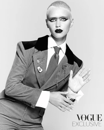 A striking black and white portrait captures a fair-skinned adult woman in a corduroy suit, gazing directly at the camera with bold makeup.