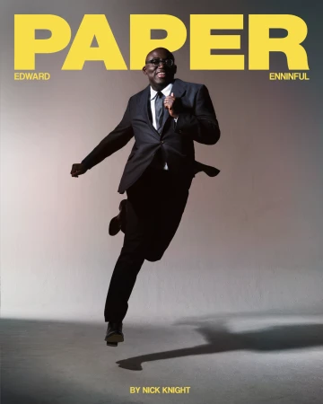 Edward Enninful leaping mid-air wearing a dark suit and tie against a plain grey studio backdrop with yellow Paper magazine masthead.