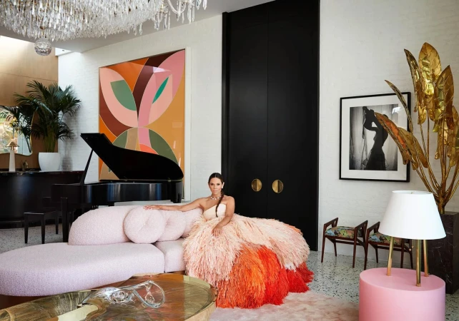 Woman in an ombre feathered gown seated on a curved pink sofa inside a modern luxury living room