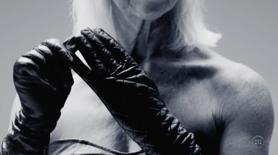 Striking black-and-white portrait of an elderly person with white hair and black leather gloves against a neutral background.