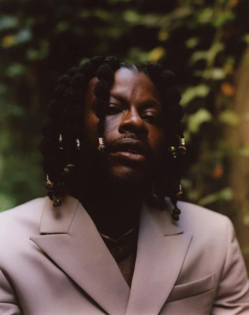 Portrait of a black man wearing a light suit jacket against a lush green foliage background