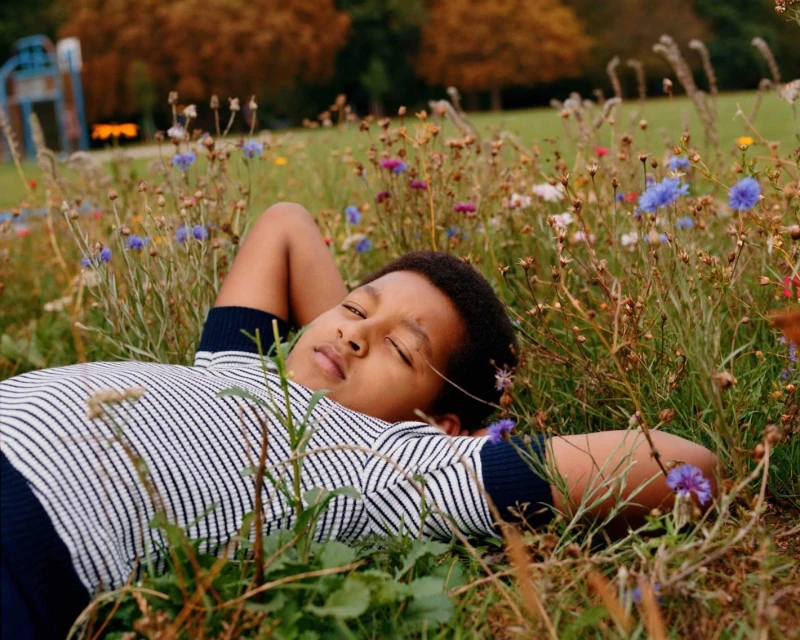 Young child rests peacefully in a meadow of colorful wildflowers, enjoying the tranquility of nature on a sunny day outdoors.