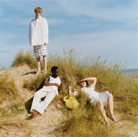 Three models posing amongst tall grass on sand dunes under a clear blue sky, styled by Adam Winder