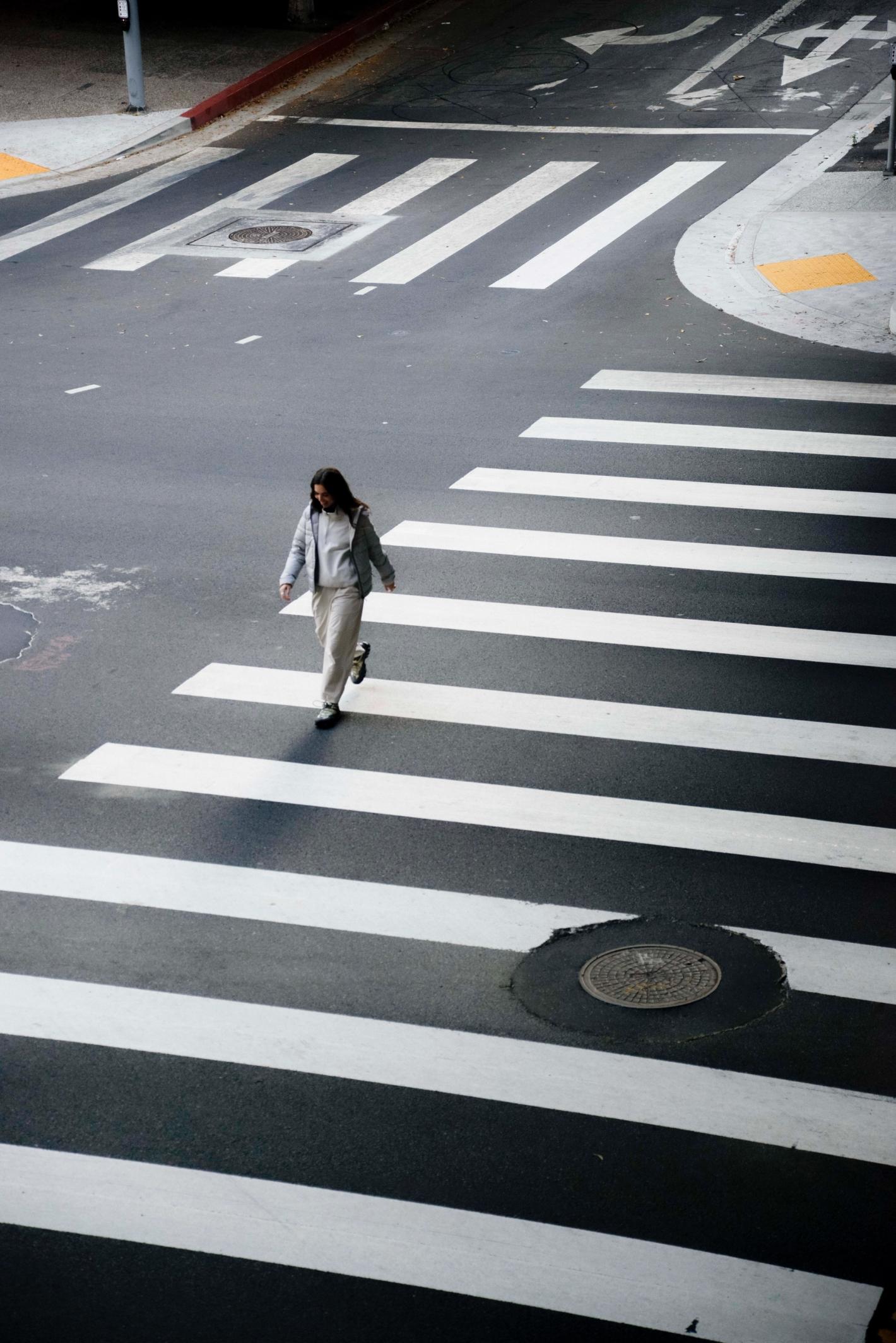 Woman in casual clothing crosses a zebra crossing in an urban setting on a sunny day, captured from a high angle view.